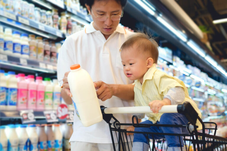 Father shows child a plastic milk jug while shopping for fresh food at the grocery store