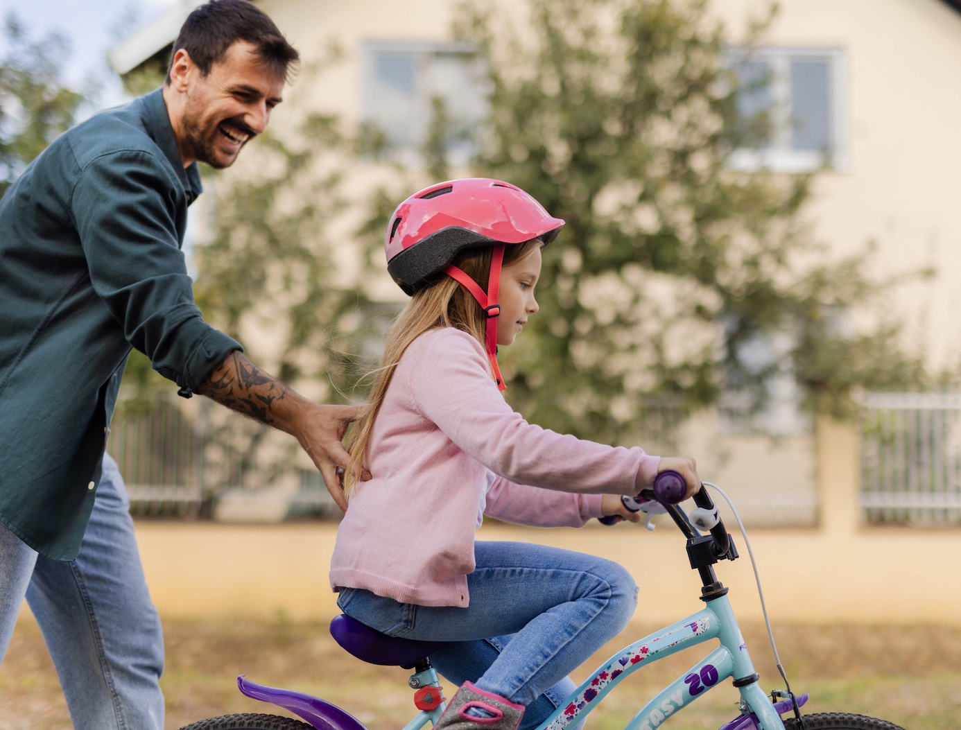Father Helps Little Daughter to Ride Bicycle on the Sidewalk in the City Suburbs