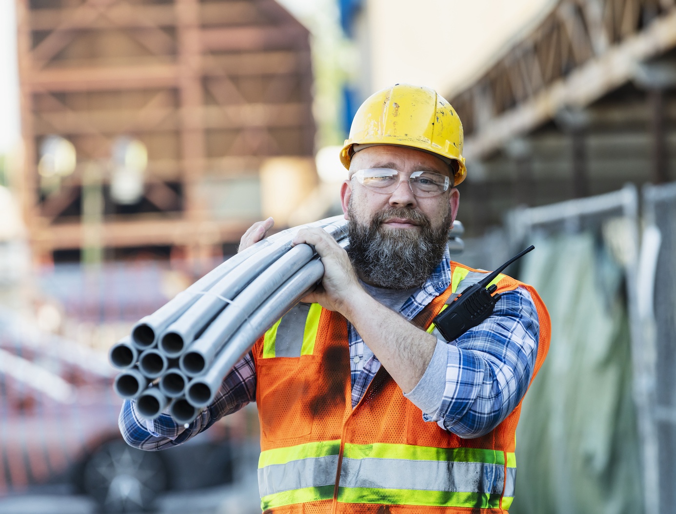 Construction worker wearing plastic protective gear carrying pipes on shoulder